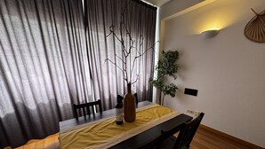 Ein Essbereich mit Tisch für zwei Personen, einer Vase mit Zweigen und einer Topfpflanze.