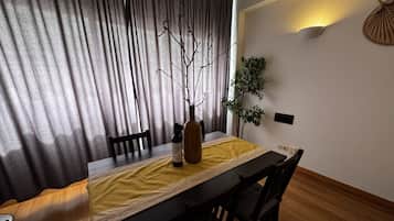 Uma área de refeições com uma mesa posta para dois, um vaso com ramos e um vaso de planta.
