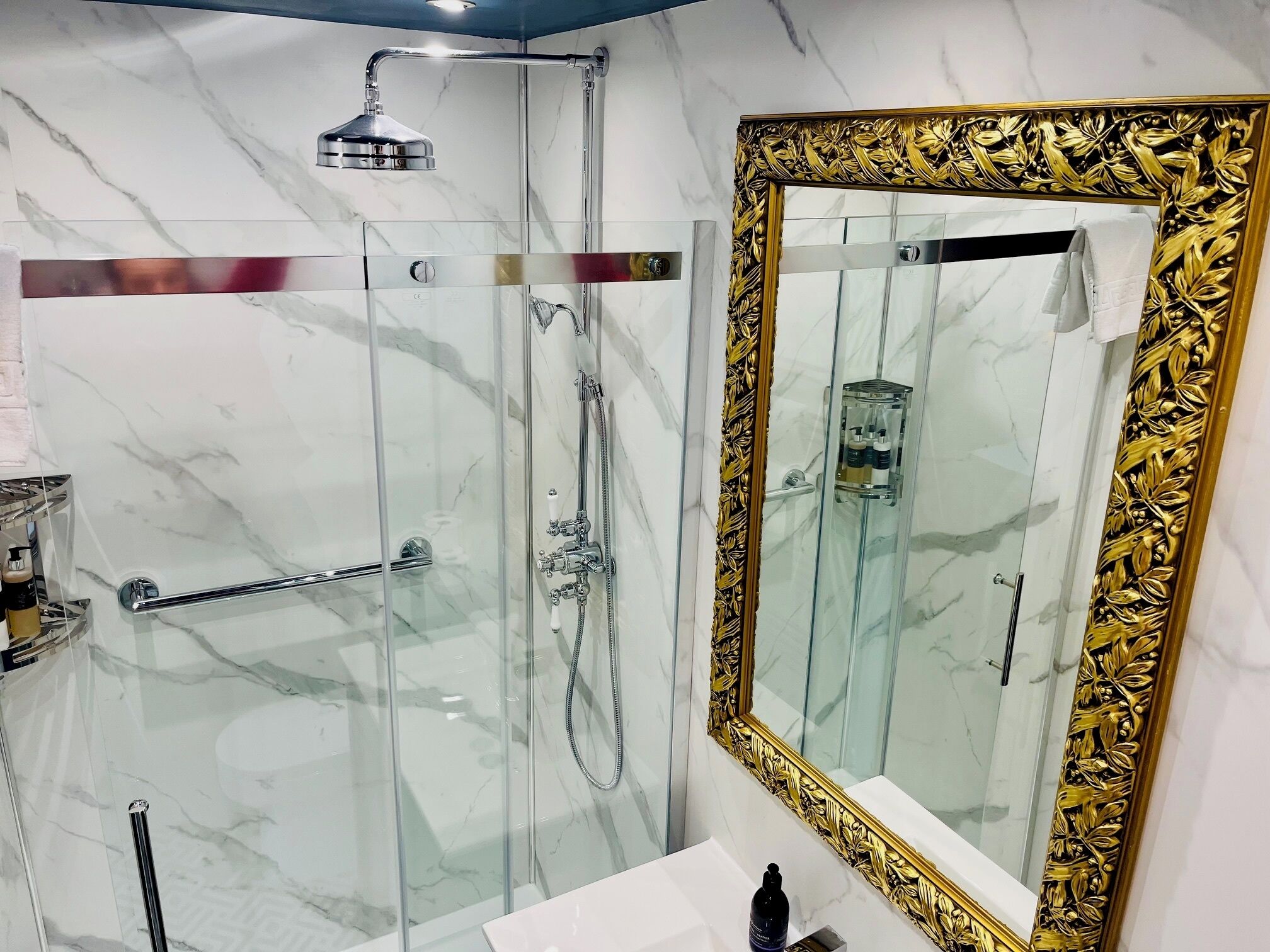 A bathroom with a glass-enclosed shower, a gold-framed mirror, and marble walls.