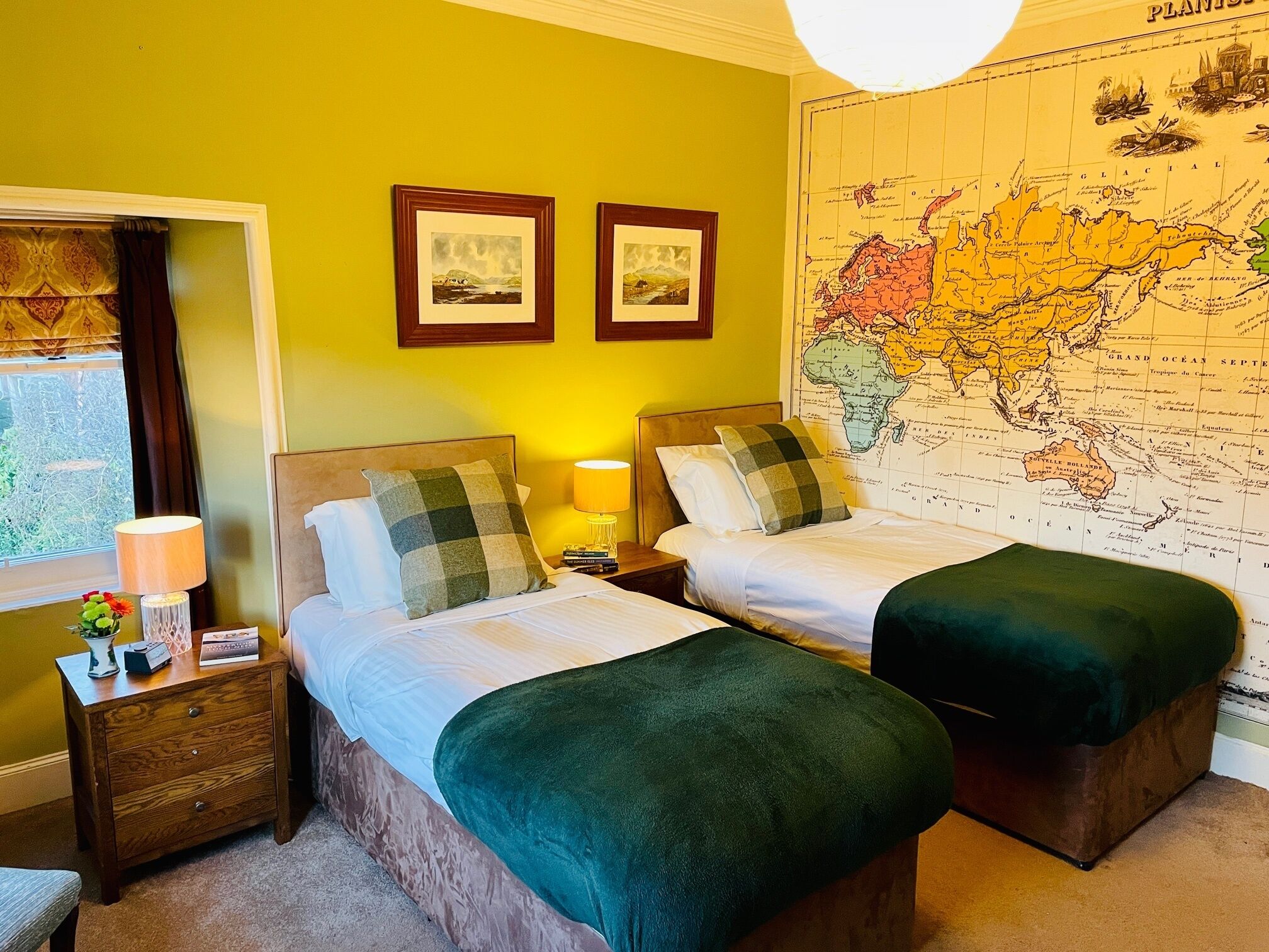 A hotel room with two beds, a map on the wall, and a window with curtains.