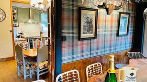 Ein Essbereich mit einem Holztisch, Korbstühlen, einer Scotch-Flasche und einem gerahmten Bild an der Wand.