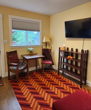 A room with a wooden chair, a small table with a vase, a bench, a television mounted on the wall, and a patterned rug. - Cozy New Studio in charming Mount Vernon, Perfect for You and Your Pup (Mount Vernon)