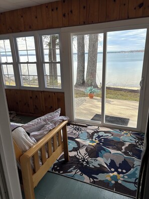 Een slaapkamer met een houten bed, uitzicht op een meer door grote ramen en een kamerkleed met patroon op de vloer.