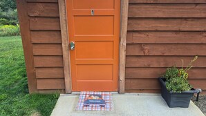 Una cabana de fusta amb una porta taronja, un estri de benvinguda i una planta en test.