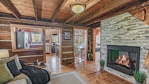 A cozy log cabin interior with a fireplace, wooden floors, and a dining area.