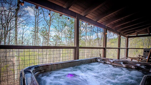 A hot tub with a view of trees through a wooden pergola.