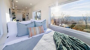 Un dormitorio con un ventanal grande, una cama con almohadas y vistas al exterior.