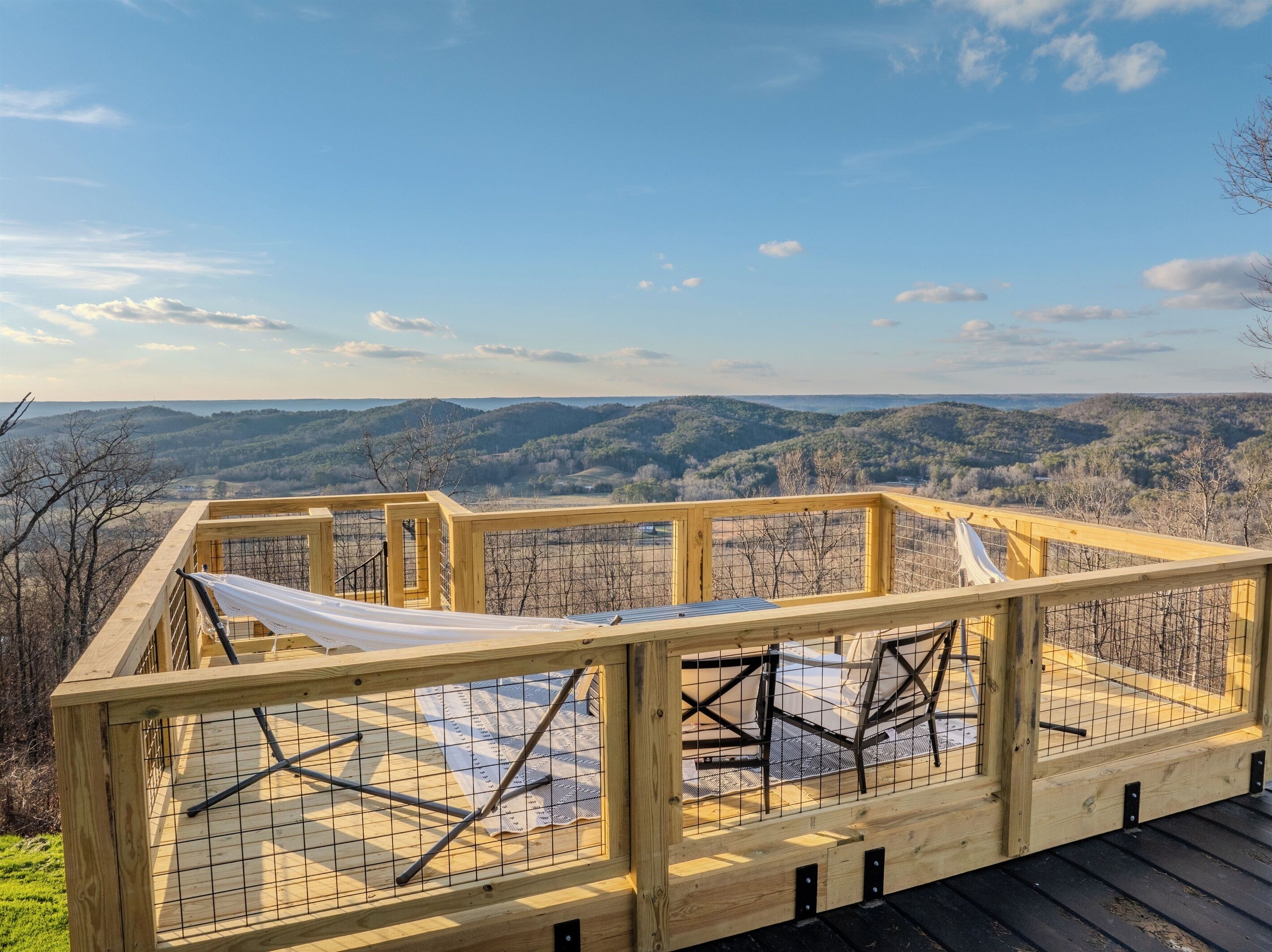 Une terrasse en bois avec un hamac et une rambarde de sécurité en métal, offrant une vue sur un paysage montagneux.