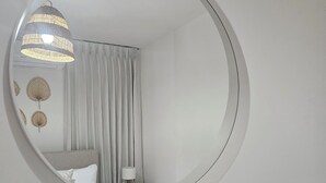 Un miroir rond est accroché au mur, au-dessus d’un lit. En dessous, on aperçoit une lampe et une petite plante.