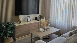 Un salon moderne avec un téléviseur à écran plat fixé au mur, une console en bois agrémentée d’objets décoratifs, un canapé et un tapis tissé.