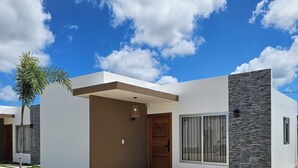 Une maison moderne à deux étages, dotée d’un toit plat, d’une entrée centrale avec une porte en bois et d’un chemin en pierre menant à la porte d’entrée.
