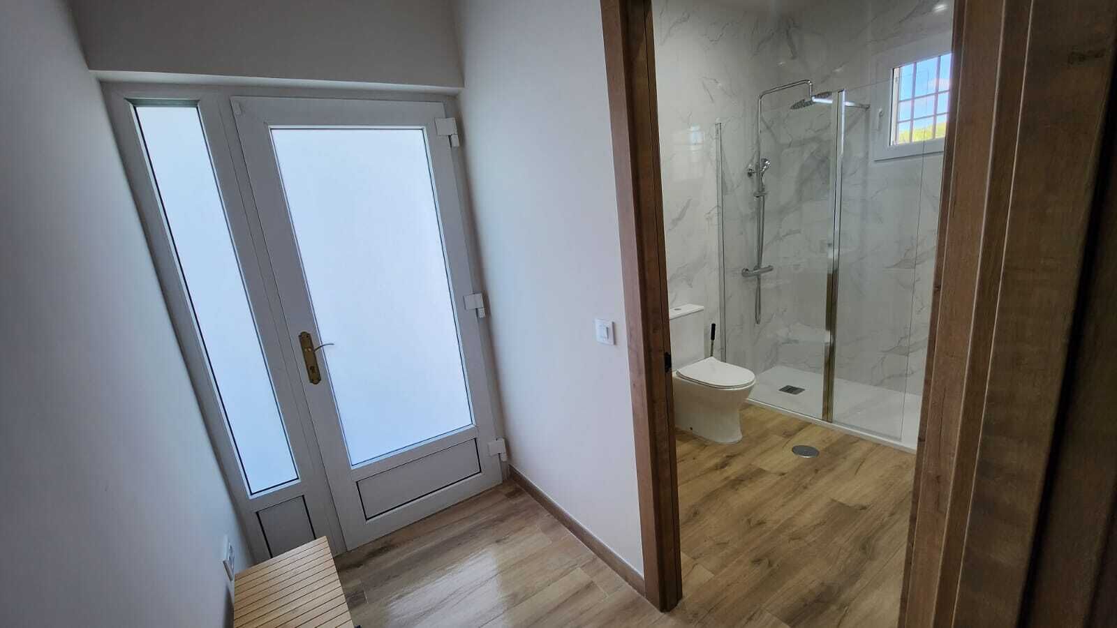 Une salle de bain avec une douche à parois de verre, des toilettes et une porte donnant sur un balcon.