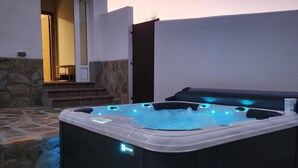 Un bain à remous doté de lumières LED bleues, un mur en pierre et une porte donnant sur une pièce.