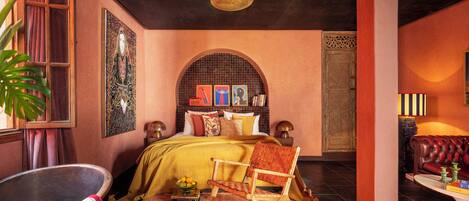 A room with a bed, a reading chair, a small table, and a large plant.