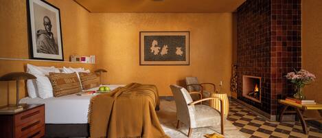 Een hotelkamer met een bed, een stoel, een open haard en een muur met een ingelijst beeld.