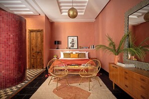 A bedroom with a checkered floor, a wooden door, a bed with pillows, a bedside table, a mirror, and a potted plant. - The Mellah Hotel (Marrakech)