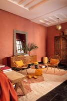 Una habitación con un espejo de cuadros, sillas de mimbre, una mesita con libros y un jarrón decorativo.