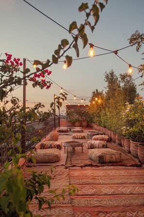 Un espacio al aire libre con luces colgantes, plantas en macetas y cojines tradicionales.