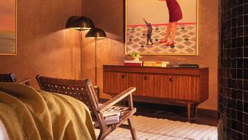 A bedroom with a bed, a desk, a chair, a lamp, and a painting on the wall.
