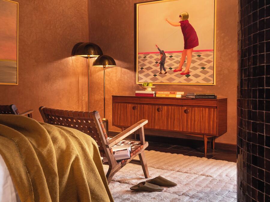 A bedroom with a bed, a desk, a chair, a lamp, and a painting on the wall.
