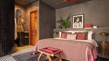 A bedroom with a bed, a bench, a mirror, a plant, and a shelf with books and a radio.