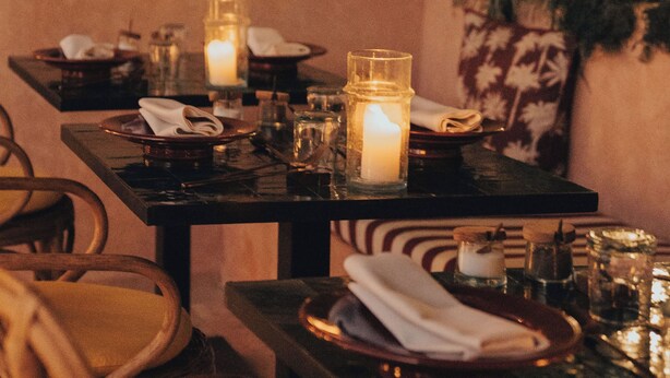 A dimly lit dining area with a table set for two, featuring candles and a potted plant. - The Mellah Hotel (Marrakech)