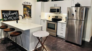 A modern kitchen with white cabinetry, stainless steel appliances, a central island with stools, and decorative plates on the wall. - Clover Street Lofts (Dallas)