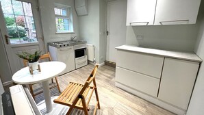 Una cuina compacta amb armaris blancs, una petita zona de menjador amb taula i cadires, i una finestra que deixa entrar llum natural.