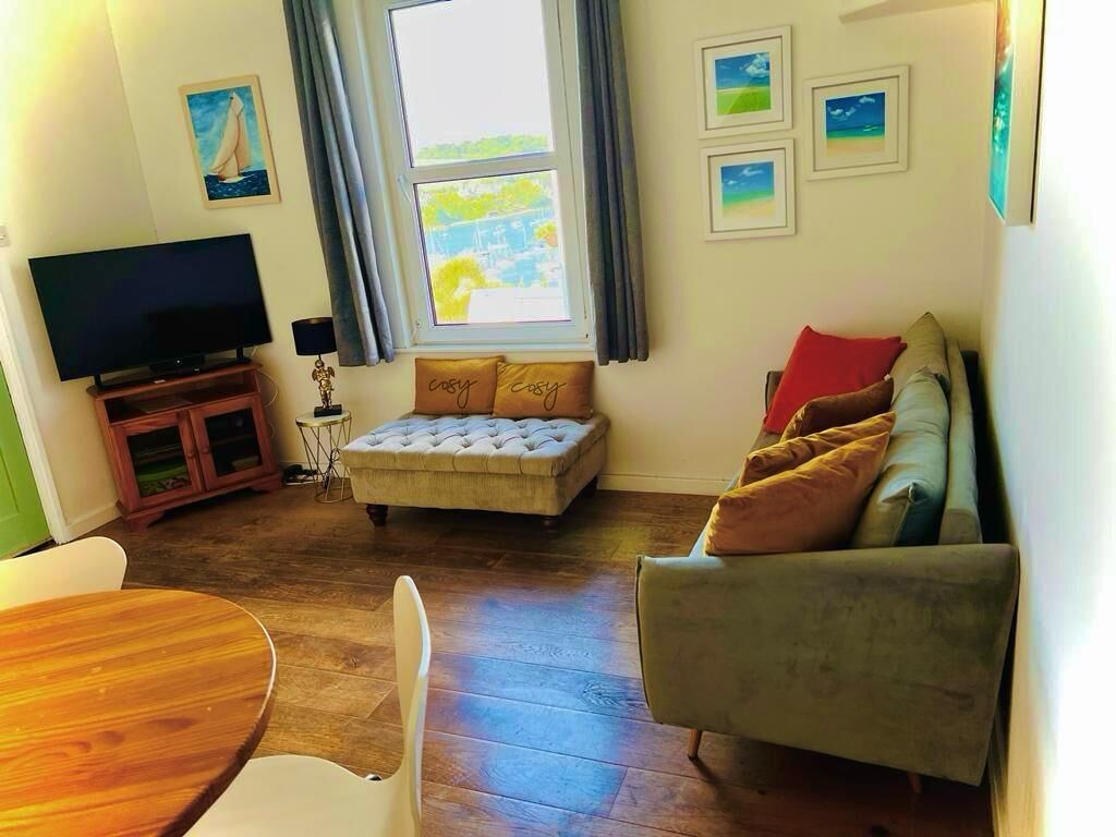 Ein gemütliches Wohnzimmer mit Fernseher, Hocker, Sofa und Esstisch.