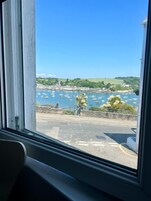 Vista de un puerto con barcos, una carretera y vegetación al fondo.