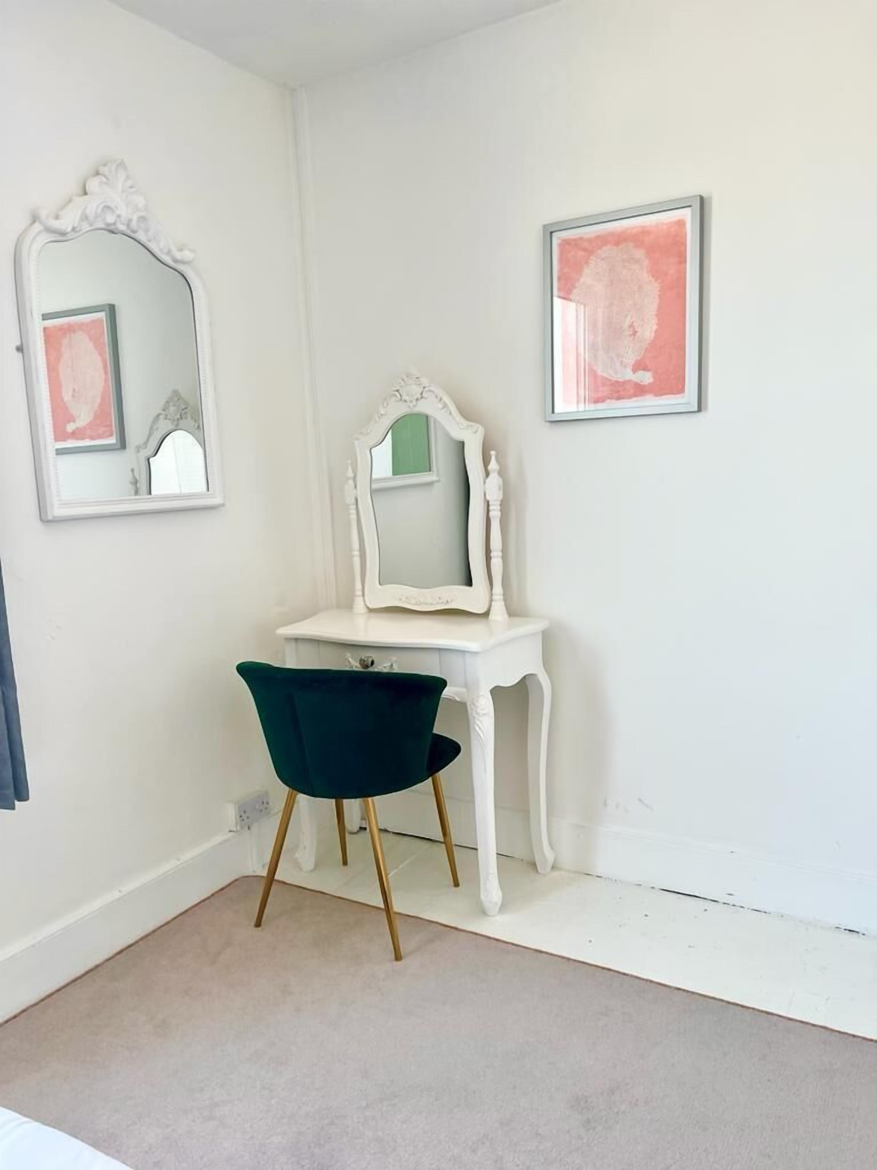 Una habitación con un tocador blanco, una silla verde y dos cuadros en la pared.