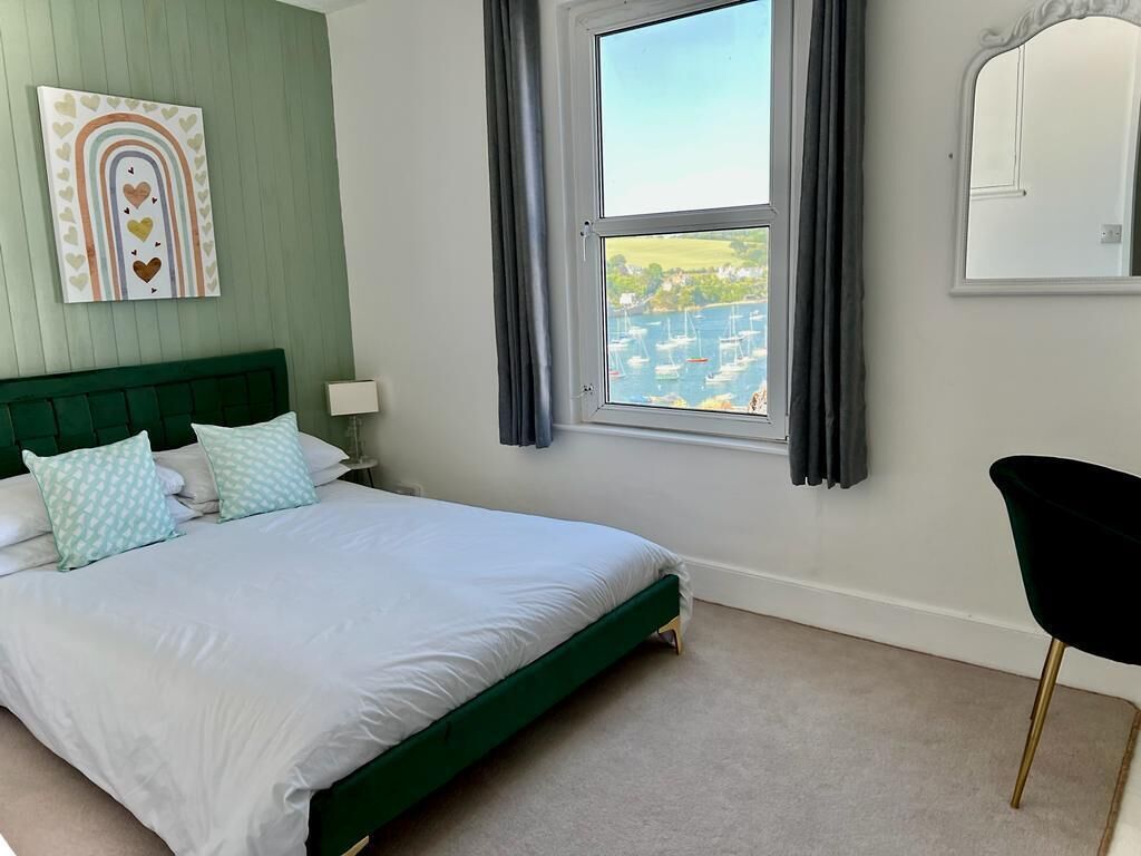 Quarto com cama verde, vista de barcos pela janela, um espelho e uma cadeira.