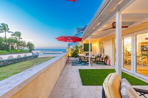 A balcony with a view of the ocean, outdoor seating, and a red umbrella.
