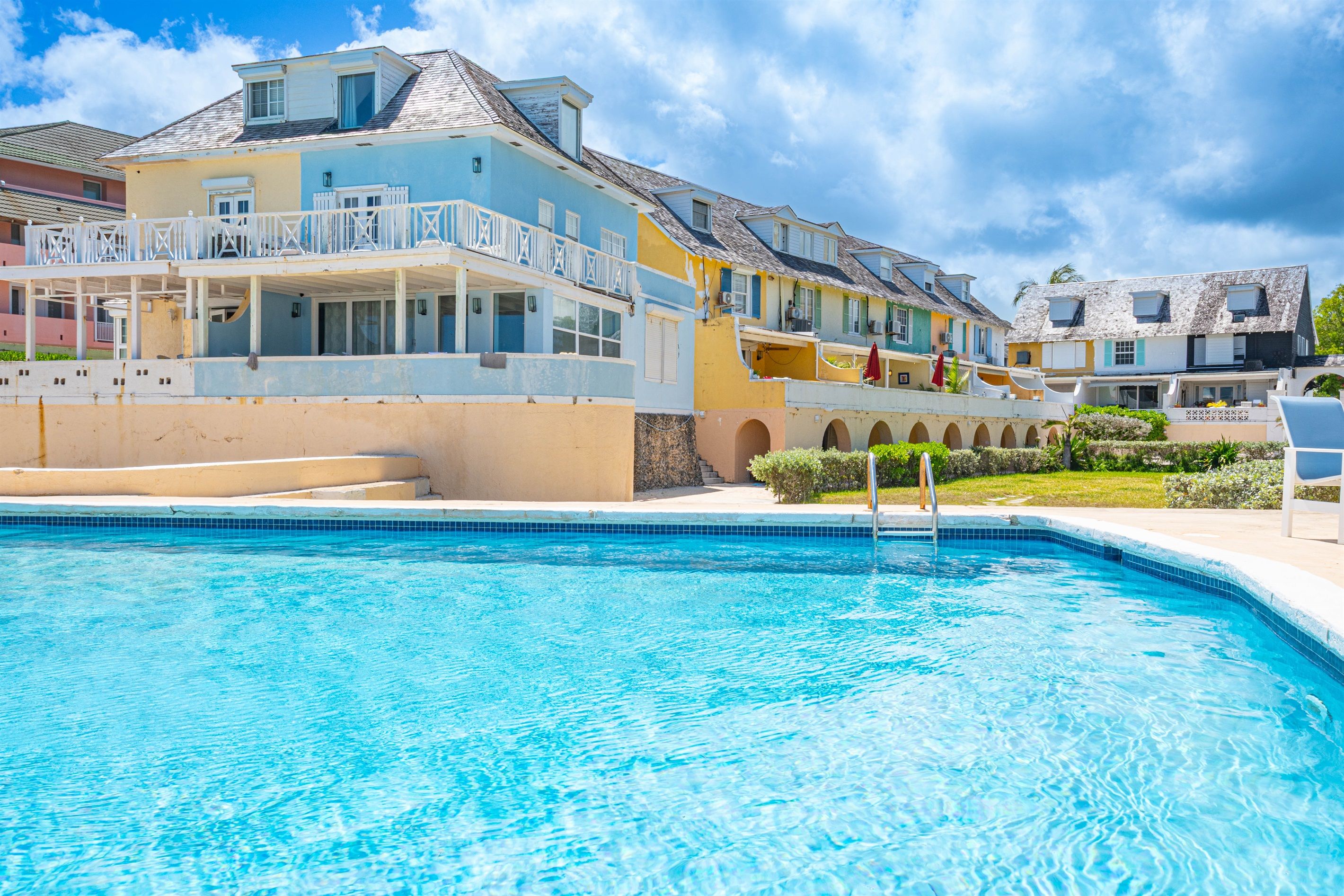 Une piscine à l’eau d’un bleu cristallin, entourée d’un bâtiment doté de balcons et d’une galerie couverte.
