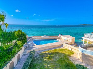 A swimming pool with a view of the ocean, surrounded by greenery and a clear sky.