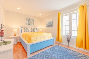 A bedroom with a bed, bedside tables, a window with curtains, and artwork on the walls.