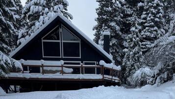 A cabin with a steeply pitched roof, large windows, and a wooden deck.