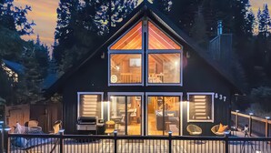 A two-story cabin with large windows, a visible kitchen area, and outdoor seating.