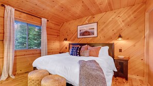 A wooden cabin bedroom with a bed, pillows, a blanket, and a picture on the wall.