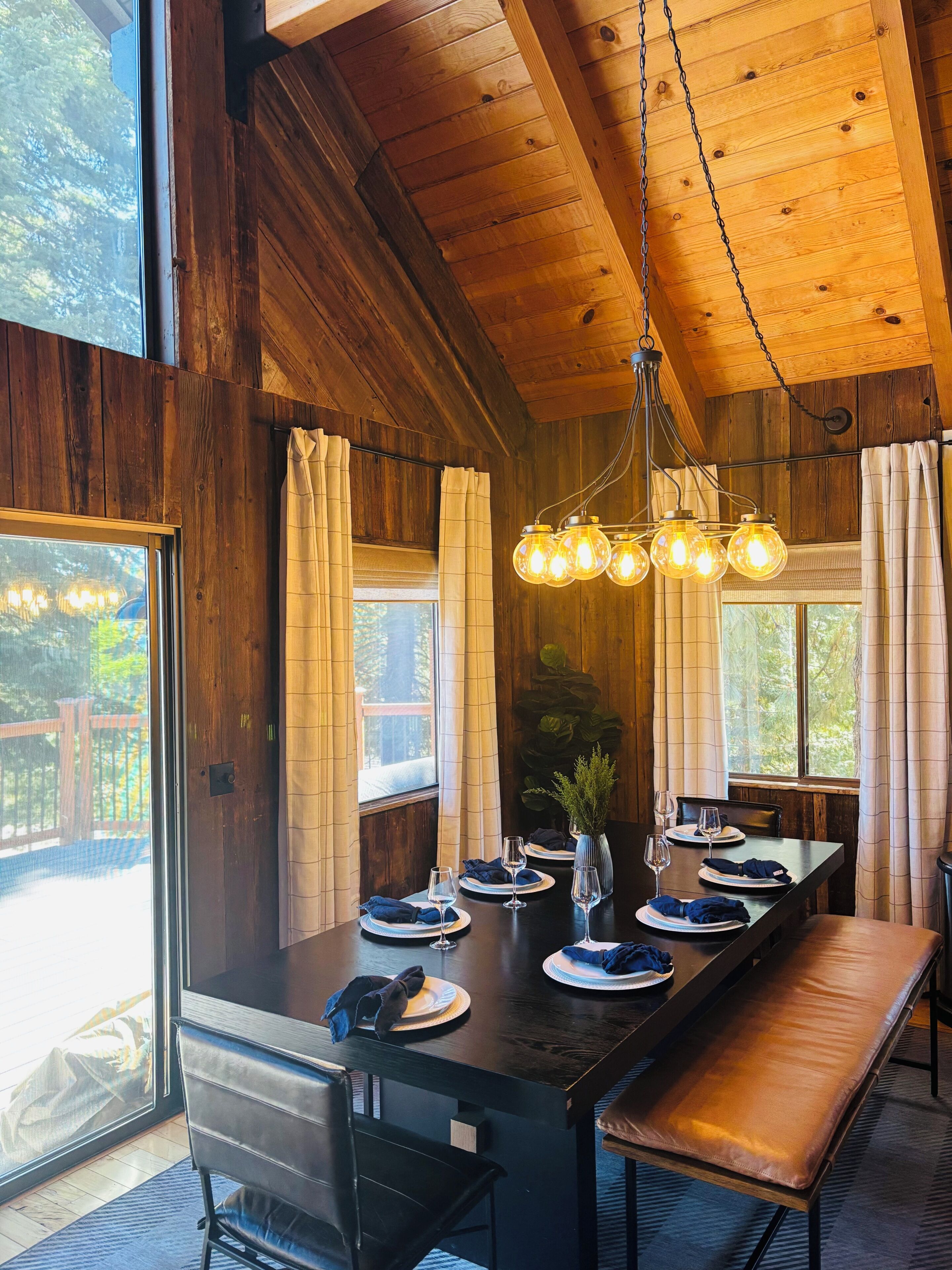 A wooden interior with a dining table set for four, a bench, and a hanging light fixture.