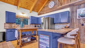 A modern kitchen with blue cabinets, a stainless steel refrigerator, and a wooden island with a sign listing cabin rules.