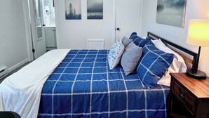 Een slaapkamer met een groot bed, een nachtkastje met een lamp en twee ingelijste foto’s aan de muur.
