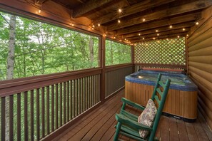 Eine Holzterrasse mit Whirlpool, Holzgeländern und Blick ins Waldgebiet.