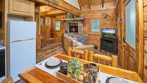 L’intérieur d’un chalet en bois comprend une cuisine, un coin repas, une cheminée et un téléviseur.