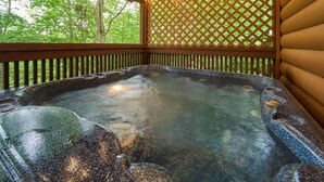 Un bain à remous doté d’une terrasse en bois et d’un mur en treillis, entouré d’arbres.