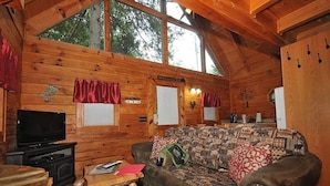 L’intérieur chaleureux d’un chalet, avec un revêtement mural en bois, un canapé, un téléviseur et une cheminée.