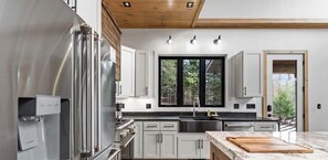 A modern kitchen with stainless steel appliances, white cabinetry, and a large window.