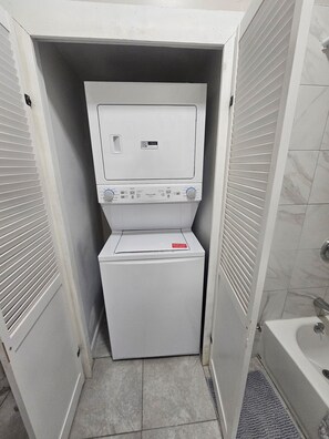 A compact laundry room with a front-loading washer and dryer, a small window, and a tiled floor.