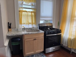 Una cocina con estufa de acero inoxidable, un lavamanos, armarios de madera y una ventana con cortinas amarillas.