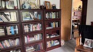 A room with a large wooden bookshelf filled with books, a framed picture, and a small statue. - Spacious river facing 4-bedroom house in charming Waldport with WiFi. (Waldport)